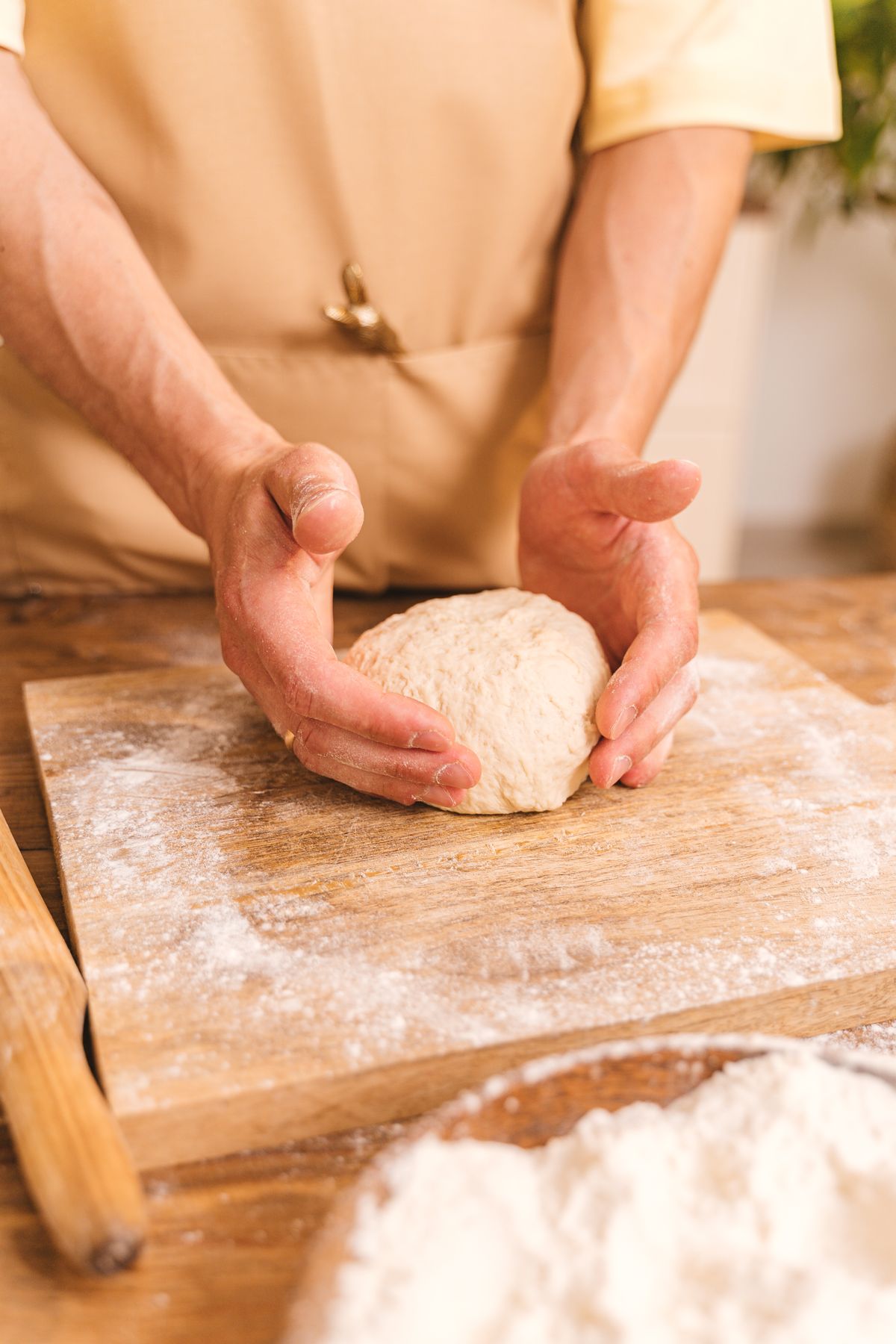 Mains qui façonnent une boule de pâte sur une planche farinée